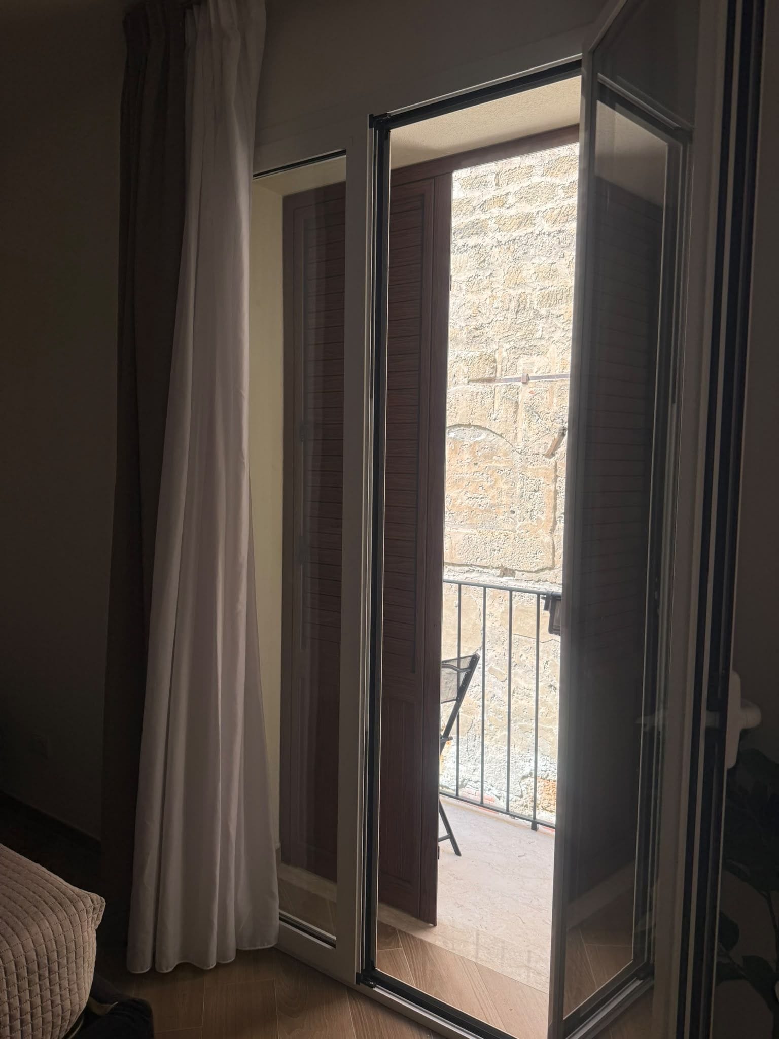 Une pièce dotée d’une porte-fenêtre coulissante donnant sur un balcon extérieur, avec un mur en pierre et une rambarde en métal.