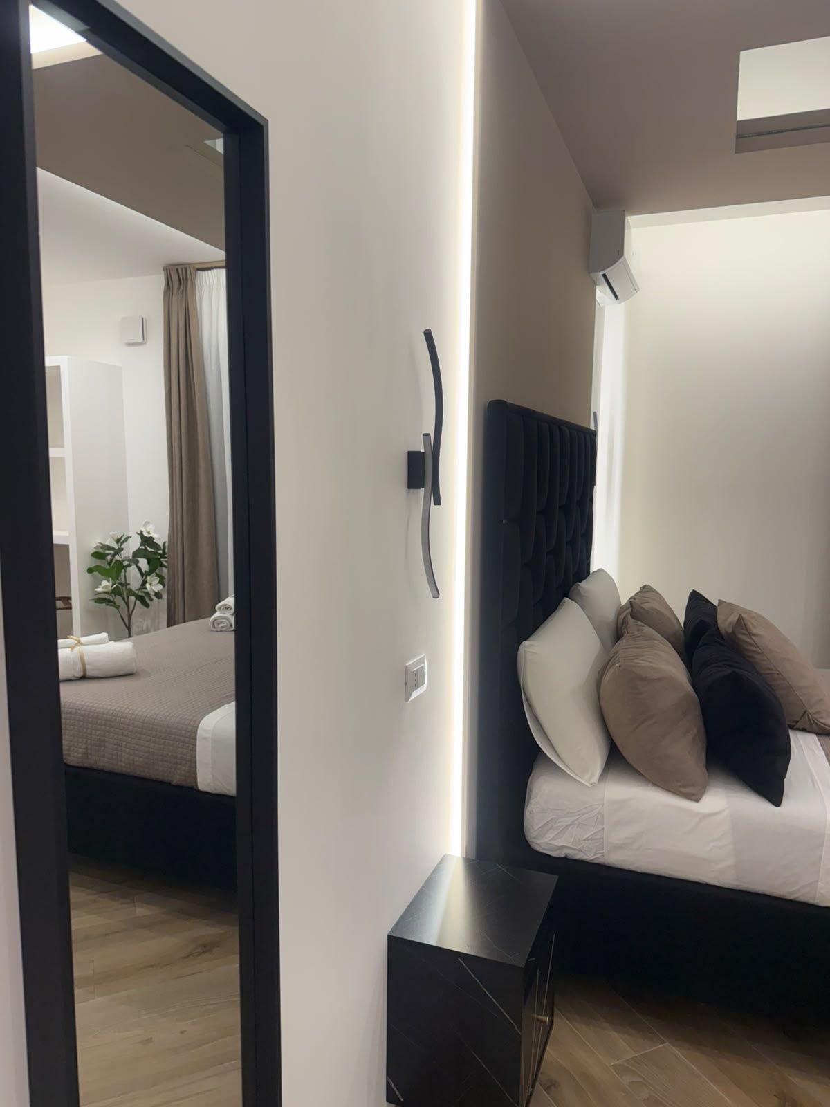 Ett hotellrum med en säng, ett nattduksbord, en spegel och utsikt över ett annat rum.