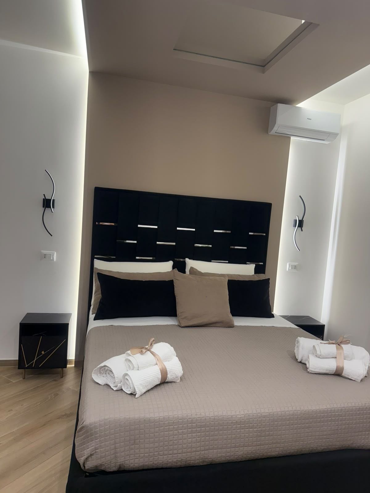 Une chambre d’hôtel moderne avec un grand lit, une tête de lit sombre et deux tables de chevet.