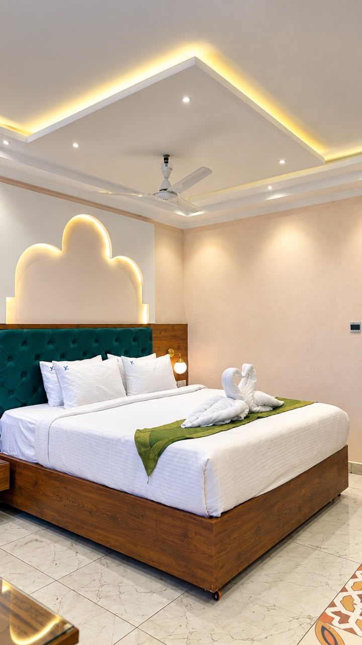 Habitación de hotel moderna con una cama grande, ventilador de techo, iluminación empotrada y un elemento decorativo en la pared.