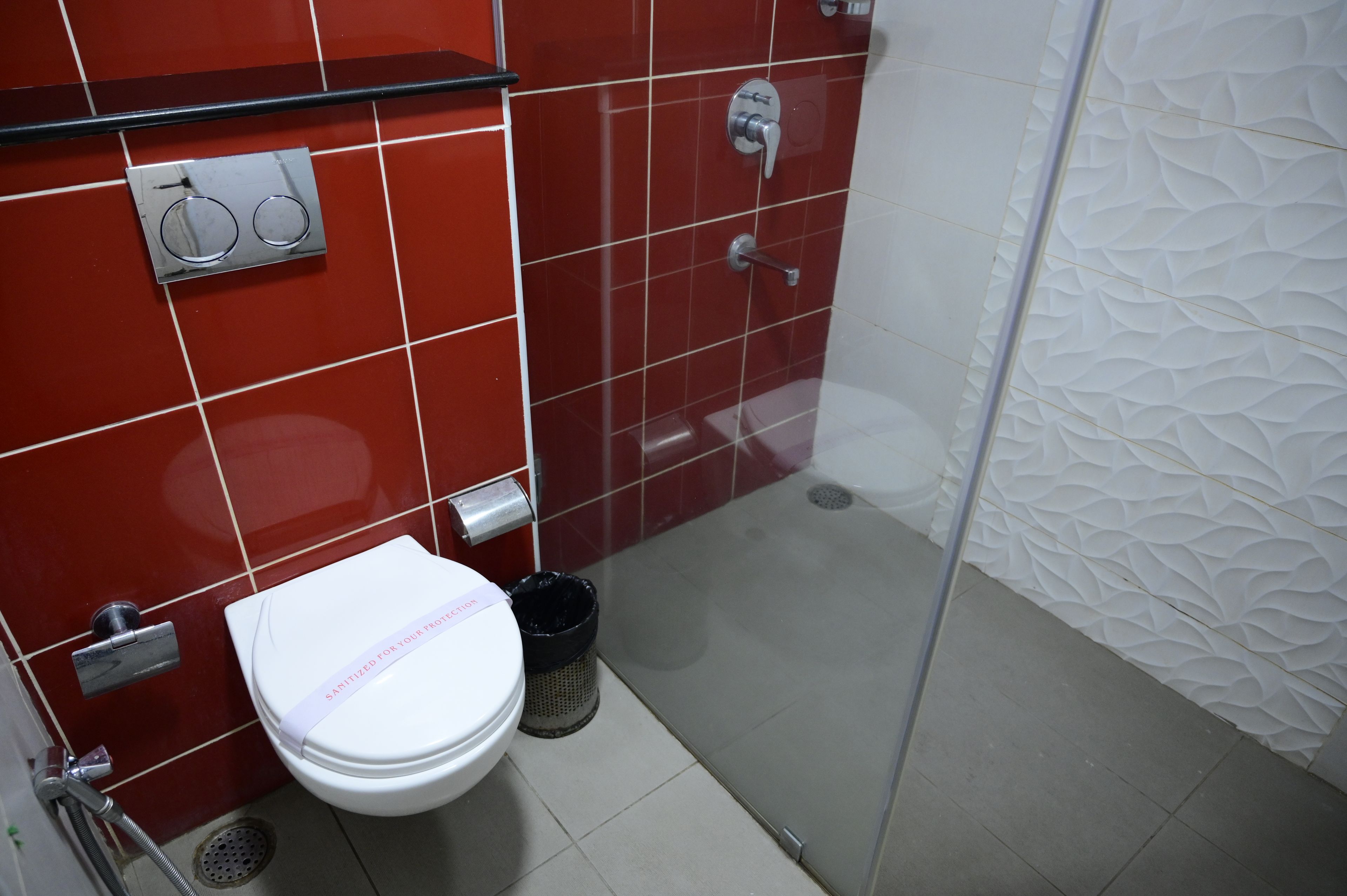 Un baño con inodoro, secamanos, cubo de basura y zona de ducha.