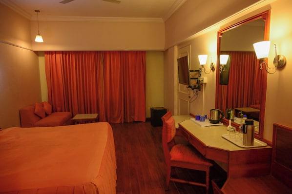 Habitación de hotel con cama, escritorio, silla, espejo y ventana con cortinas.