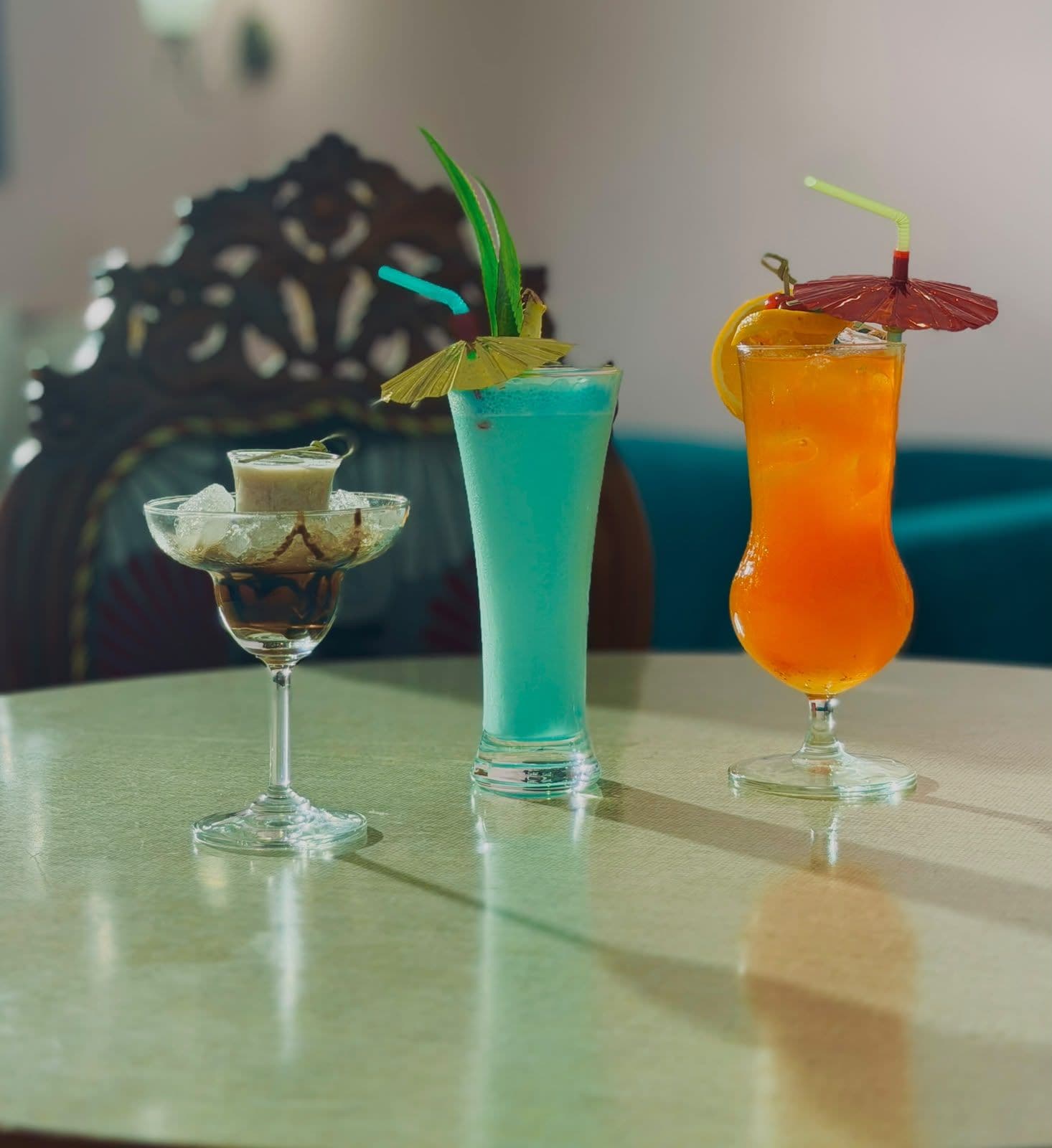 Tres bebidas sobre una mesa, con una silla decorativa al fondo.