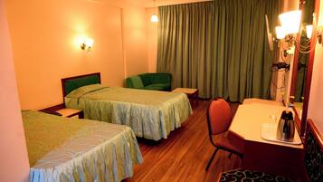 Camera d'albergo con due letti singoli, una scrivania con sedia, un tavolino e una grande finestra con tende.