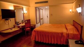 Habitación de hotel con cama, escritorio con silla, televisión y baño visible a través de una puerta abierta.