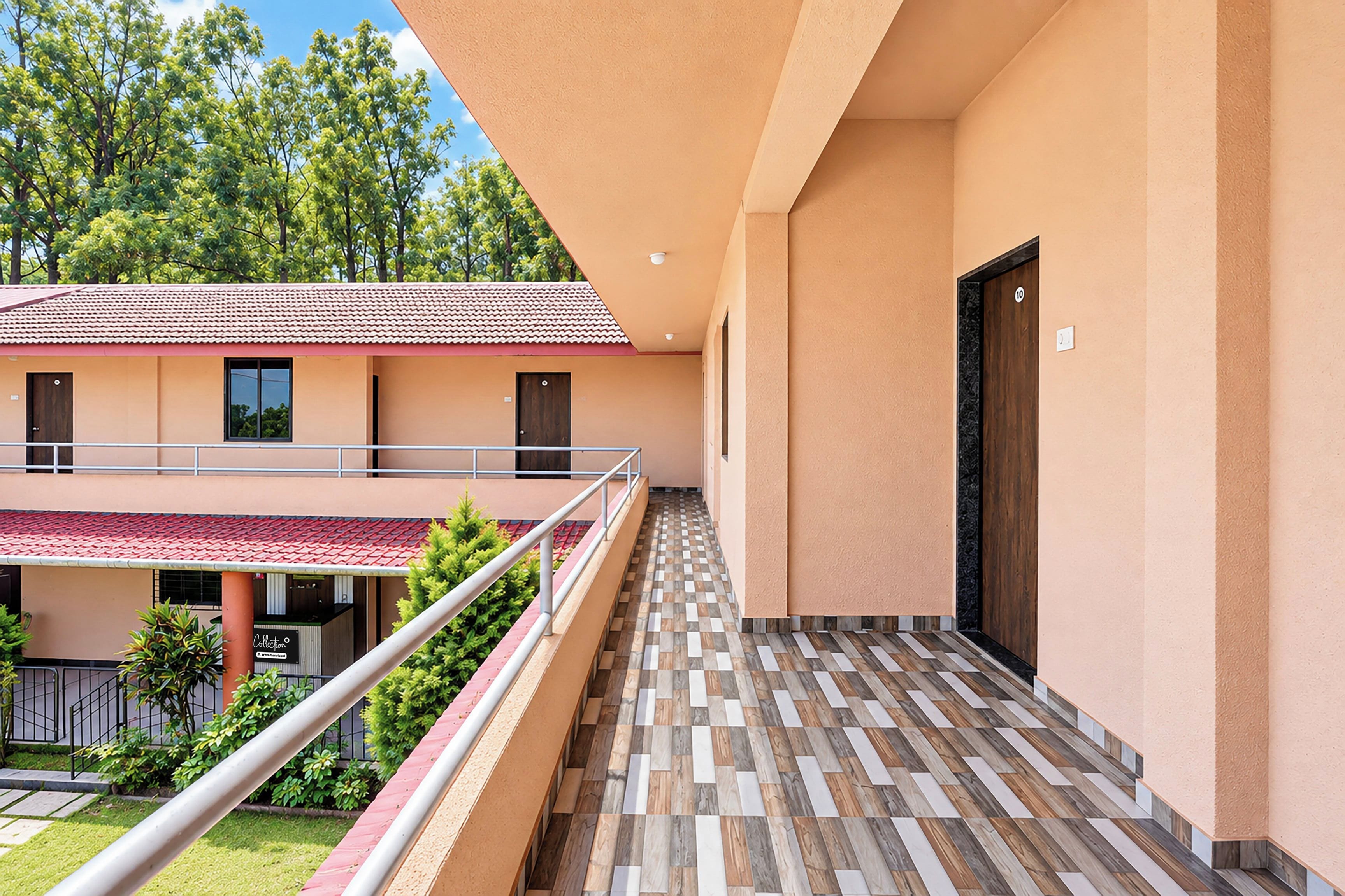 A hotel corridor with a tiled floor, a balcony with a metal railing, and a building with a red-tiled roof in the background.