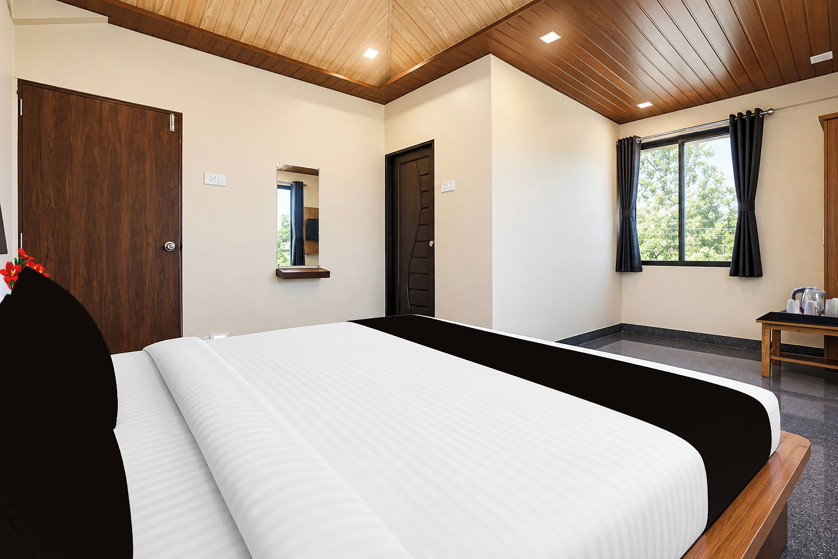 Una habitación de hotel con una cama grande, techo de madera, ventana con cortinas y una pequeña mesa con tetera.