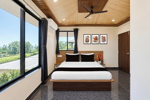 Un dormitorio moderno con una cama grande, un ventilador de techo y vistas a un paisaje verde por la ventana.