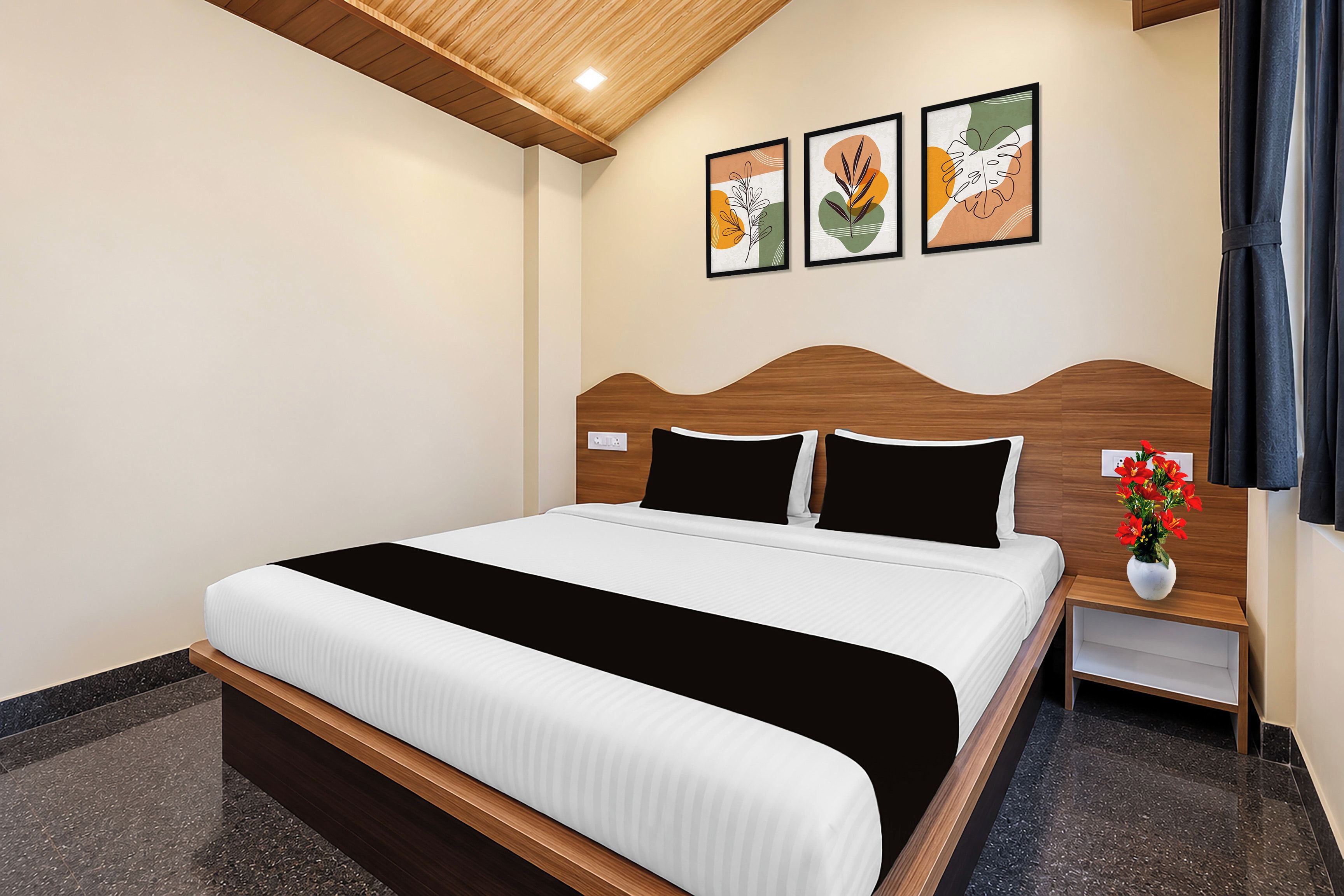Une chambre d’hôtel avec un lit, une table de chevet, un vase de fleurs et trois œuvres d’art encadrées accrochées au mur.