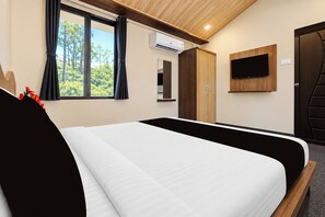 Habitación de hotel con cama, televisor montado en la pared, equipo de aire acondicionado y ventana con cortinas.