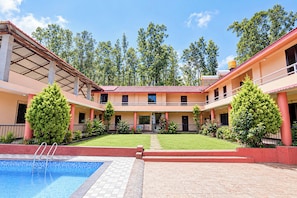 Pátio de hotel com piscina, gramado central e edifício de dois andares com varandas.