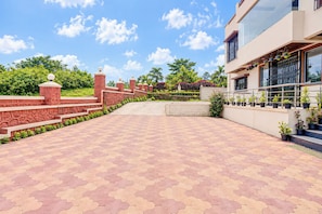 A paved walkway leading to a building with a modern design, a gated entrance, and a variety of potted plants.