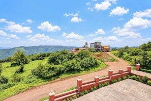 A hilly landscape with a paved path leading to a building with multiple stories and a flat roof. - Collection O Sunset Point Pangari (Mahabaleshwar)