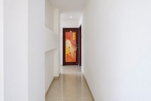 Un pasillo con una puerta al final, paredes blancas y suelo de baldosas.