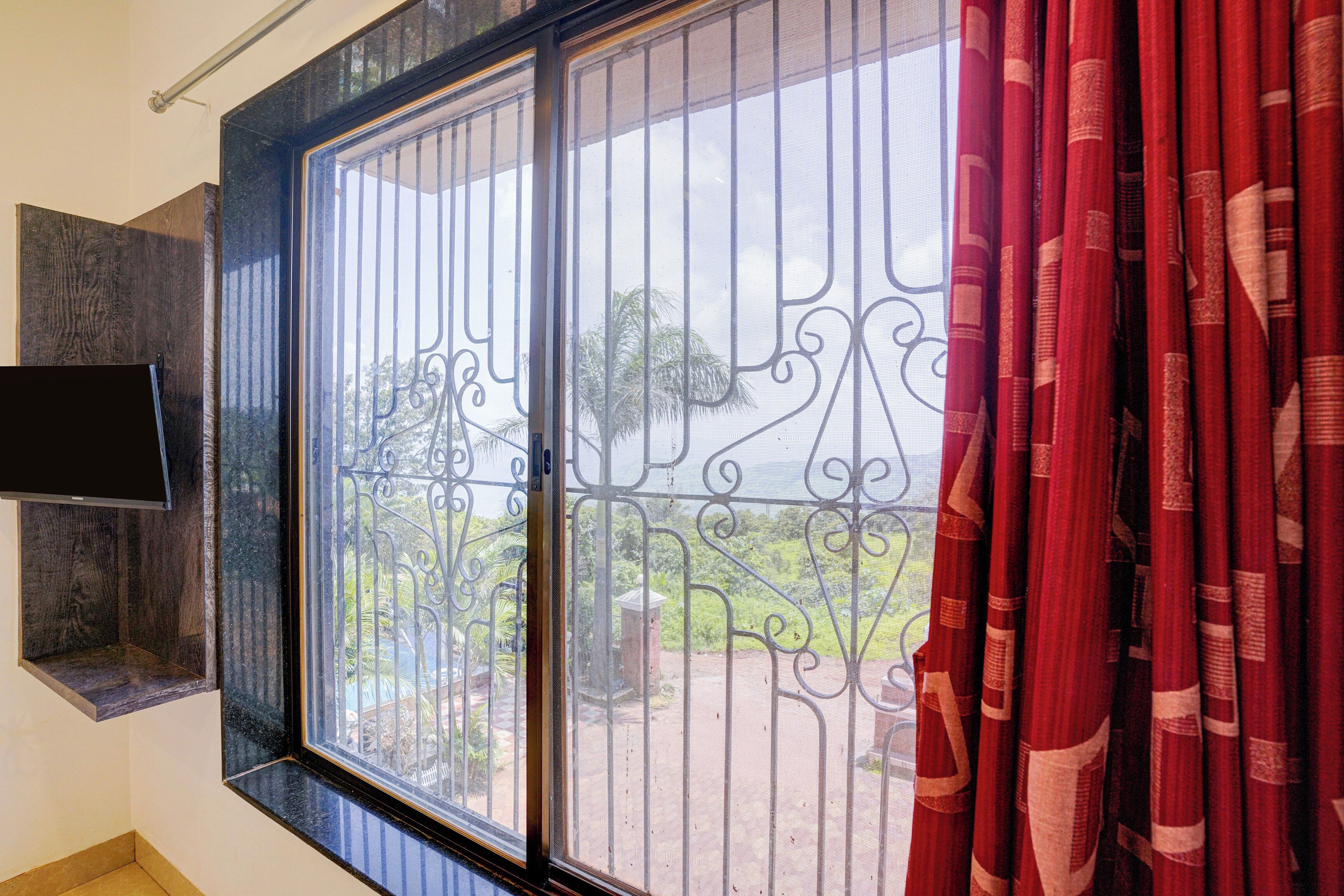 A room with a large window, a television mounted on the wall, and a red curtain.