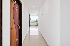 A hallway with a wooden door, a fire extinguisher, and a view of a balcony with a chair.