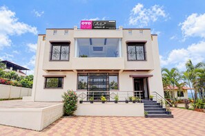 A modern two-story building with a flat roof, large windows, and a sign advertising an app. - Collection O Sunset Point Pangari (Mahabaleshwar)