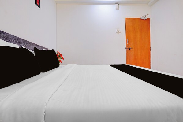 A hotel room with a bed, a wooden door, and a wall-mounted light fixture. - Collection O Sunset Point Pangari (Mahabaleshwar)