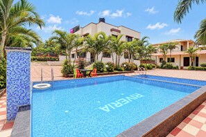 Una piscina con borde de azulejos, rodeada de palmeras y un edificio con techo de tejas.
