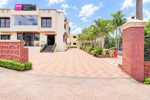 A hotel entrance with a paved walkway, palm trees, and outdoor seating. - Collection O Sunset Point Pangari (Mahabaleshwar)