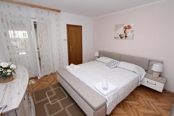 Ein Schlafzimmer mit einem Bett, Nachttischen, einer Bank, einer Tür und einer Wand mit einem Gemälde.