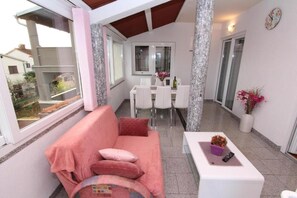 Ein Balkon mit einer rosa Couch, einem Esstisch mit Stühlen und einem Topfpflanzen.