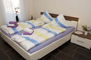 A neatly made bed with striped bedding, a bedside table with a vase and a bottle, and a nightstand with a drawer. - Holiday apartment Sonnenidyll, Borkum (Borkum)