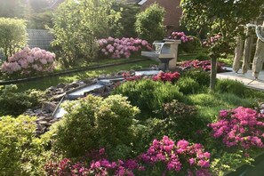 A garden with a water feature, lush greenery, and pink flowers. - Holiday apartment Sonnenidyll, Borkum (Borkum)