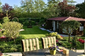 A patio with a table and chairs, surrounded by a well-maintained garden and a small house with a red roof. - Holiday apartment Sonnenidyll, Borkum (Borkum)