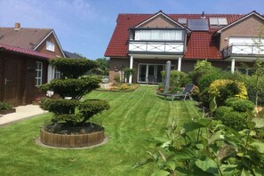 A residential property with a well-maintained lawn, a patio area with outdoor furniture, and a brick house with a red roof. - Holiday apartment Sonnenidyll, Borkum (Borkum)