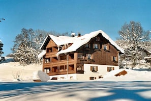 A multi-story wooden chalet with a snow-covered roof, surrounded by a snowy landscape. - Holiday apartment with 2 bedrooms (Oberstdorf)