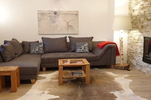 A living room with a sectional sofa, a coffee table, a fireplace, and a wall-mounted painting. - Holiday apartment with 2 bedrooms (Oberstdorf)