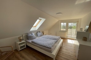 A bedroom with a sloped ceiling, a skylight, a bed with patterned bedding, bedside tables, a chair, and a view through a window. - Country House Maarweg (Loquard)
