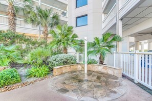 A courtyard with a stone fountain, palm trees, and a white fence. - Galveston Condo - 2nd-Floor Coastal Retreat with a Shared, Year-Round Heated Pool (Galveston)
