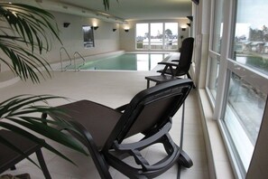Een binnenzwembad met uitzicht op buiten, een zithoek met stoelen en een potplant.