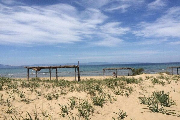 Ein Strand mit zwei hölzernen Strukturen, vermutlich Sitzbereiche, und spärlicher Vegetation.