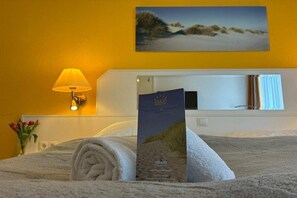 Ein Hotelzimmer mit einem Bett, einer Lampe, einem gerahmten Bild an der Wand und einer Broschüre auf dem Bett.
