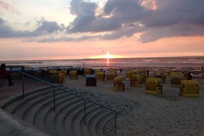 Een strand met gele strandstoelen en een trap die naar het zand leidt.