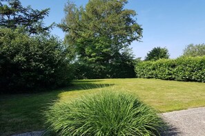 A well-maintained lawn with a variety of shrubs and a large tree providing shade. - Holiday home Burhave (Burhave)
