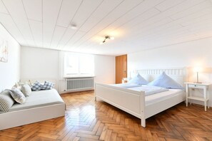 A bedroom with a white bed, a white sofa, and a wooden floor. - C - Dinkelbach Object 1 (Lindau)