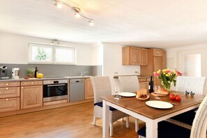 A modern kitchen with wooden cabinets, a dining table set for two, and a window providing natural light. - C - Dinkelbach Object 1 (Lindau)