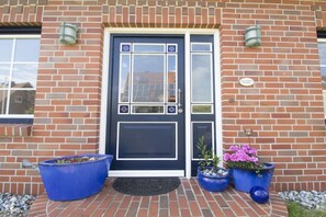 A brick building with a dark blue door, two large potted plants, and a small sign on the wall. - Holiday home in Juist with swimming pool (Juist)