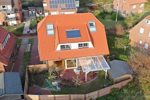 Uma casa residencial com telhado inclinado, quintal cercado e um painel solar visível no telhado.