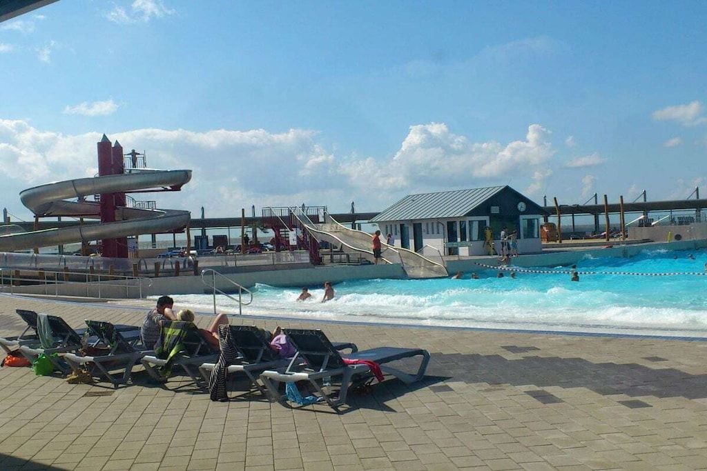 Un área de piscina con un tobogán de agua, sillas de descanso y un edificio de techo inclinado.