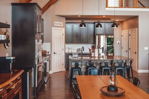 A modern kitchen with dark cabinets, stainless steel appliances, and a central island with bar stools. - Hidden Meadows | Hocking Hills, Sleeps 14, Hot Tub (Rockbridge)