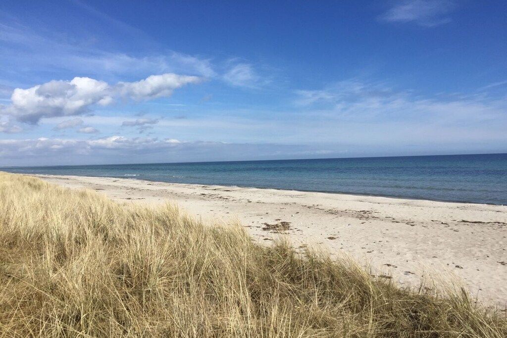 A beach with sand and grass in the foreground and a clear sky.