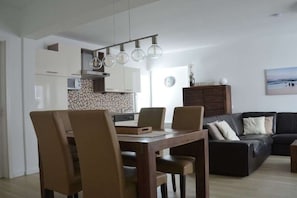 A modern kitchen with a dining area, a sofa, and a clock on the wall. - Holiday apartment with 2 bedrooms (Borkum)