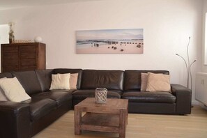 A living room with a dark brown leather sofa, a wooden coffee table, and a beach-themed painting on the wall. - Holiday apartment with 2 bedrooms (Borkum)