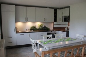 A modern kitchen with white cabinets, a dining table with chairs, and a microwave. - Holiday apartment with 3 bedrooms (Weißenstadt)
