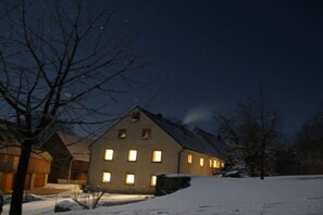 Schneebedeckte Landschaft mit einem Haus, das viele Fenster und ein geneintes Dach hat.